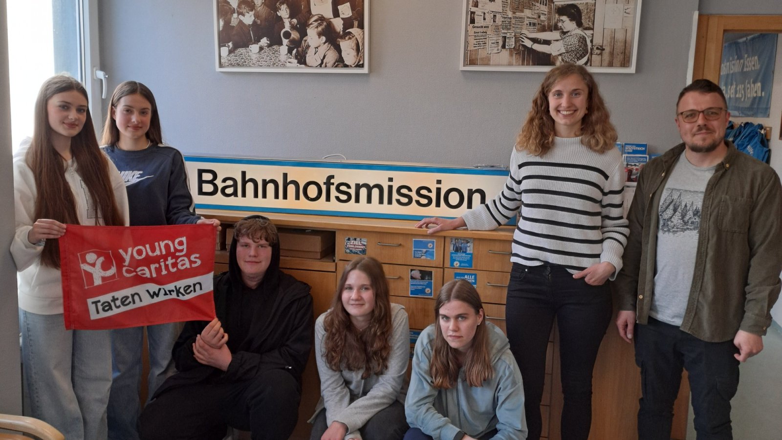 6 Personen stehen um das Schild der Bahnhofsmssion 