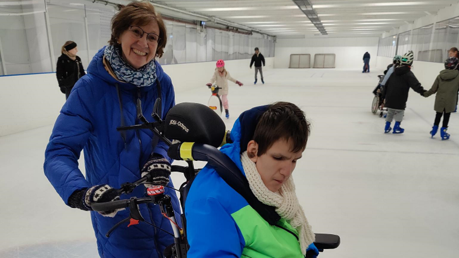Ehrenamtliche und Jugendlicher im Rollstuhl auf der Eisbahn