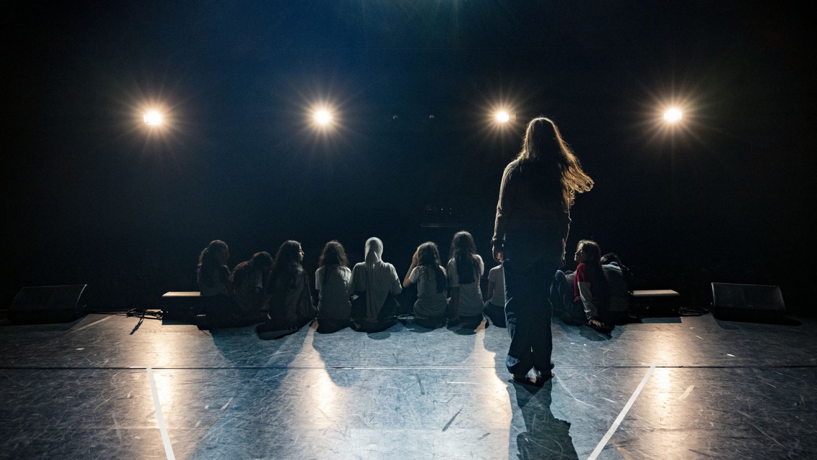 Jugendliche sitzen auf Theaterbühne uns sehen im Gegenlicht ins Publikum