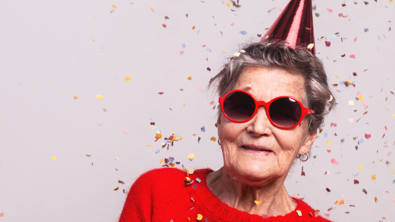 Eine ältere Dame mit Partyhut auf dem Kopf und Konfetti