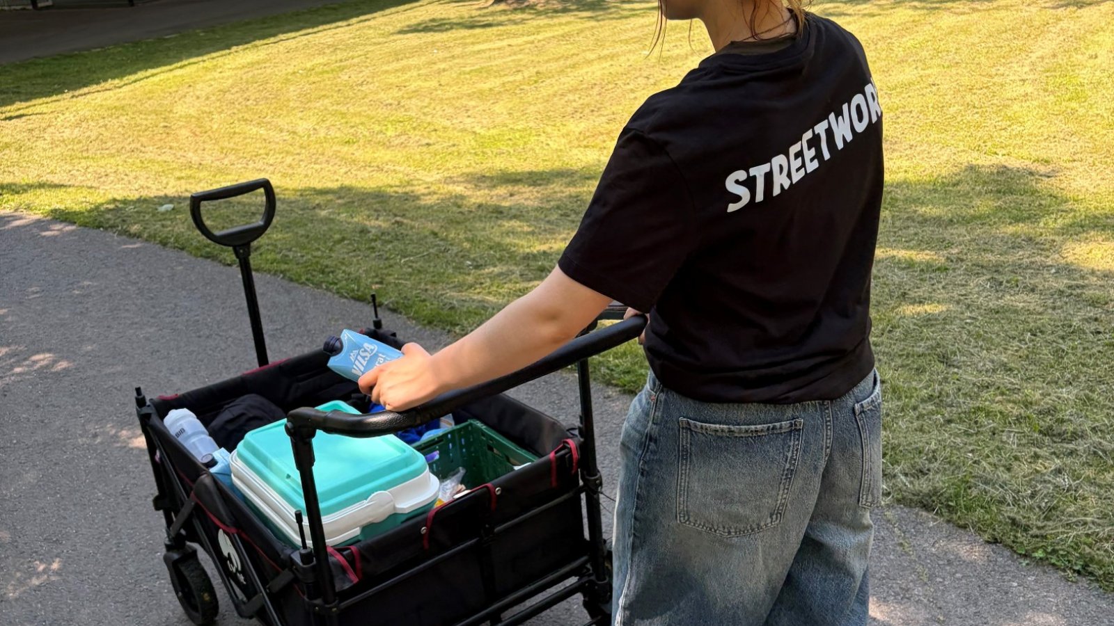 Rückansicht eine:r Streetworker:in mit Bollerwagen